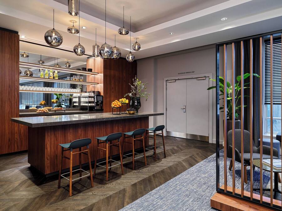 Una cocina moderna con una isla central, taburetes de bar, iluminación colgante y vistas al área de estar a través de una puerta corredera.