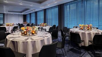 Un comedor de hotel con mesas redondas dispuestas para seis comensales, cada una con mantel blanco, sillas negras y centros de mesa florales.
