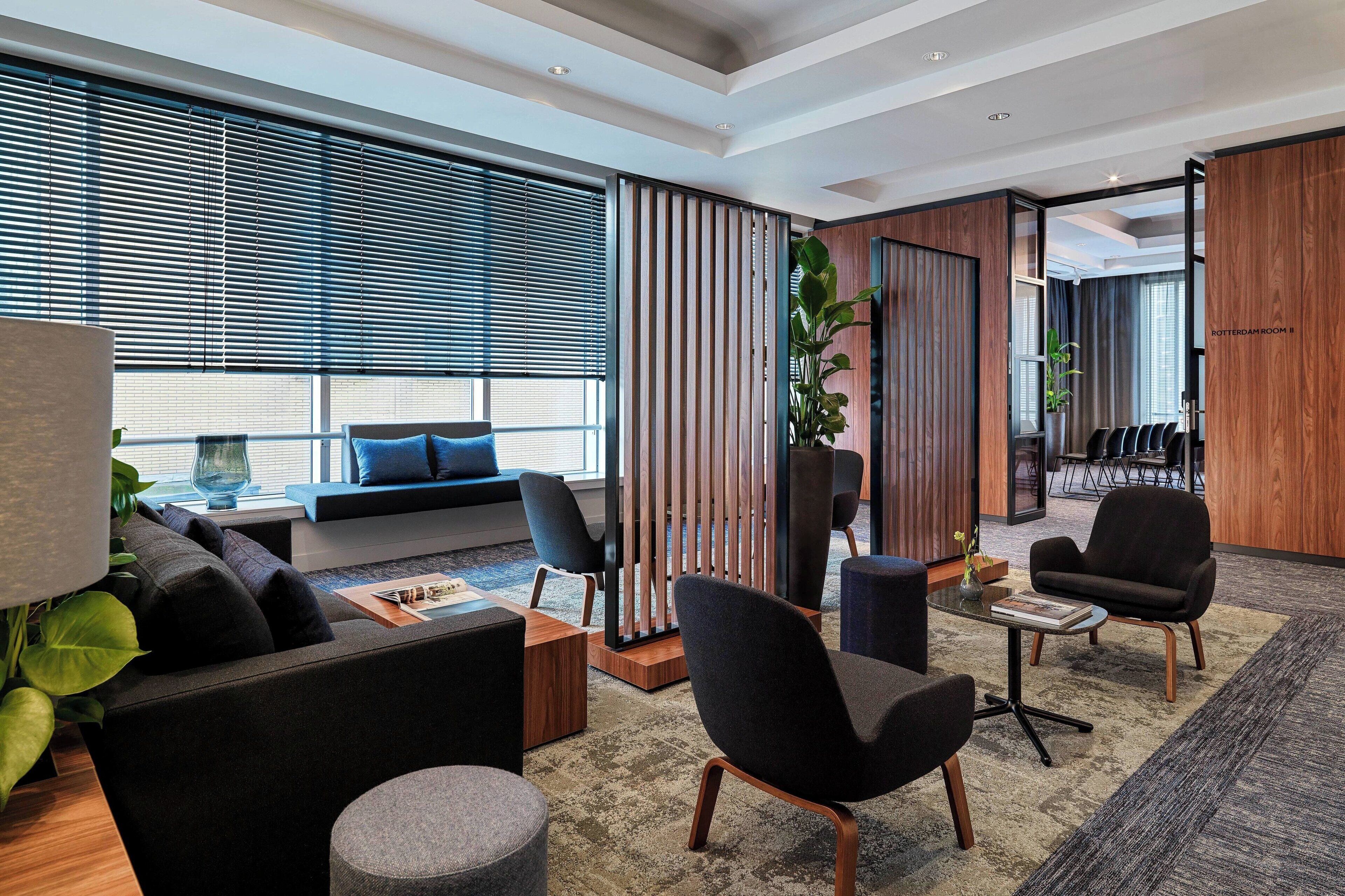 A modern office space with a sofa, chairs, a coffee table, and a large window with blinds.
