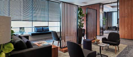 A modern office space with a sofa, chairs, a coffee table, and a large window with blinds.