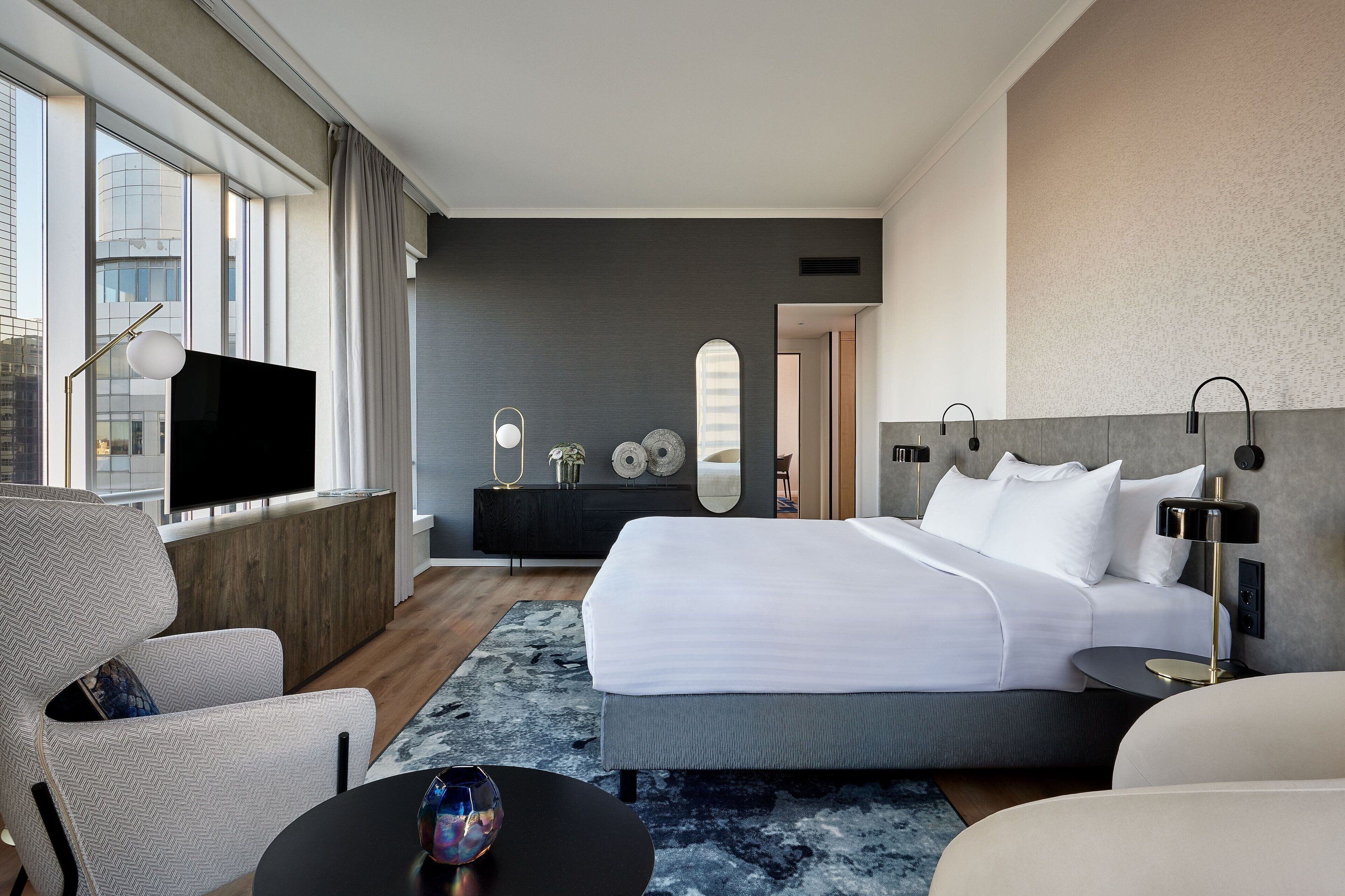 Ein modernes Hotelzimmer mit einem großen Bett, einem Fernseher, einer Couch und einem Schreibtisch.