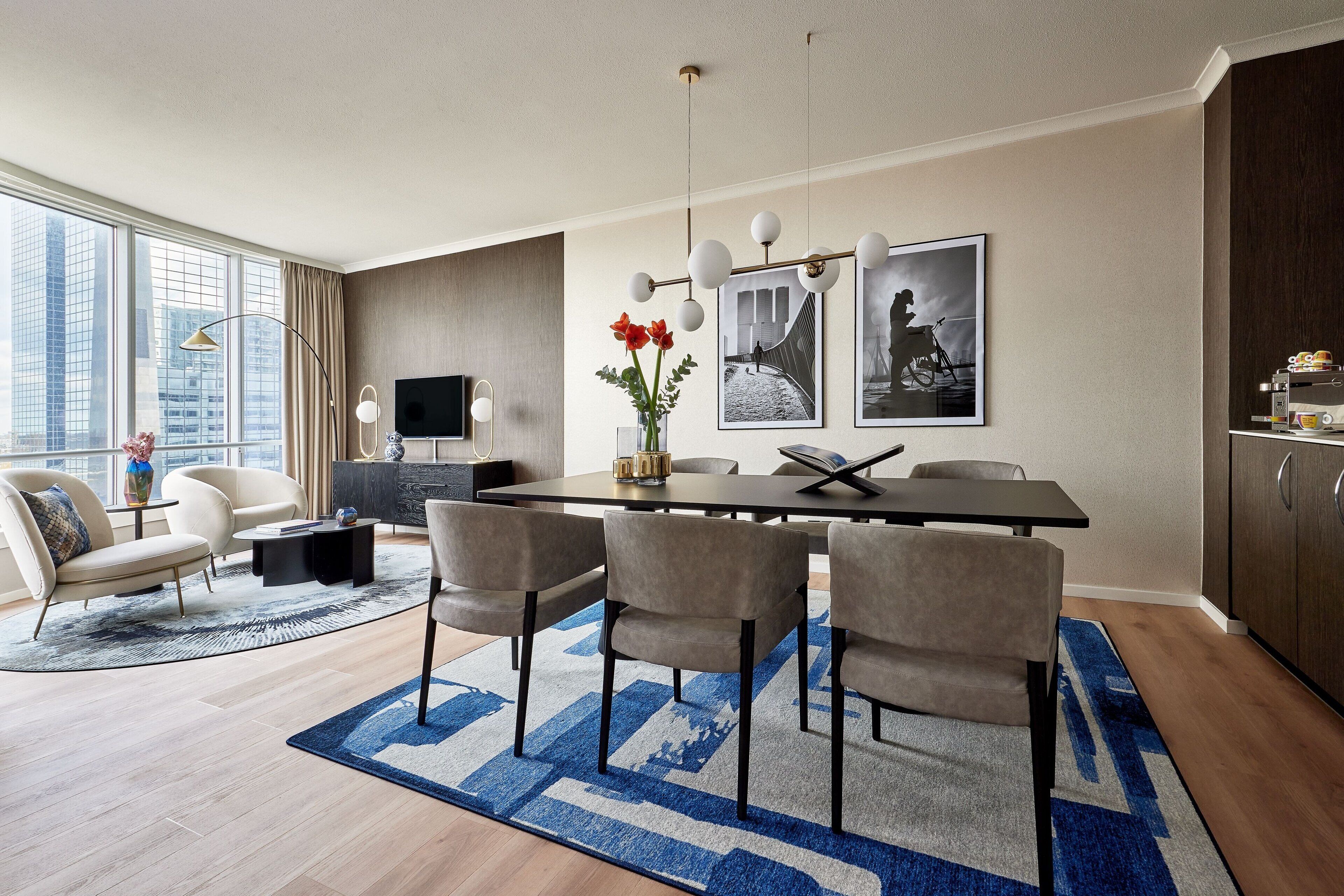 Un espace repas moderne avec une grande table, six chaises, un vase rempli de fleurs rouges et des tableaux encadrés accrochés au mur.