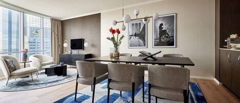 Un espace repas moderne avec une grande table, six chaises, un vase rempli de fleurs rouges et des tableaux encadrés accrochés au mur.
