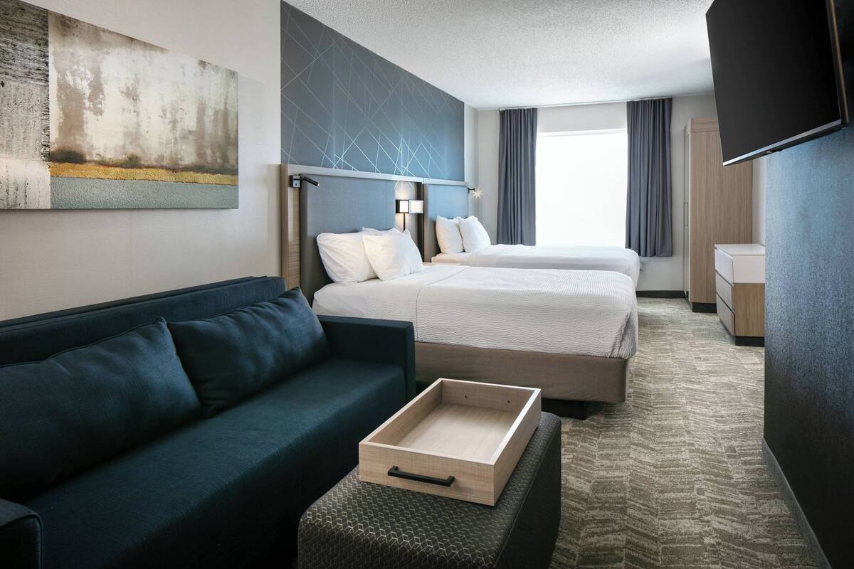A hotel room with a bed, a sofa, a TV, and a painting on the wall.