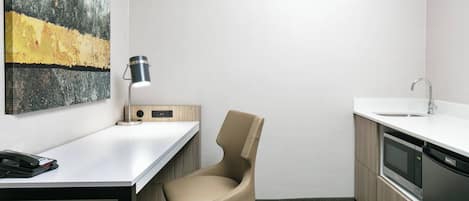 Een moderne kantoorruimte met een bureau, stoel, lamp en een keukenhoek met een magnetron en vaatwasser.