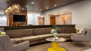 Eine moderne Lobby mit Ecksofa, Sesseln, einem runden Couchtisch und Pendelleuchten.