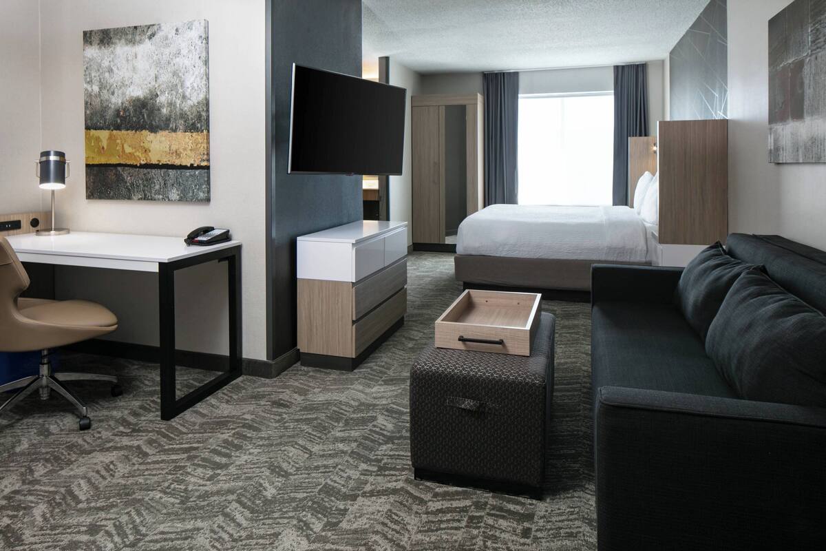 A modern hotel room with a bed, a desk with a computer, a TV, and a sofa.