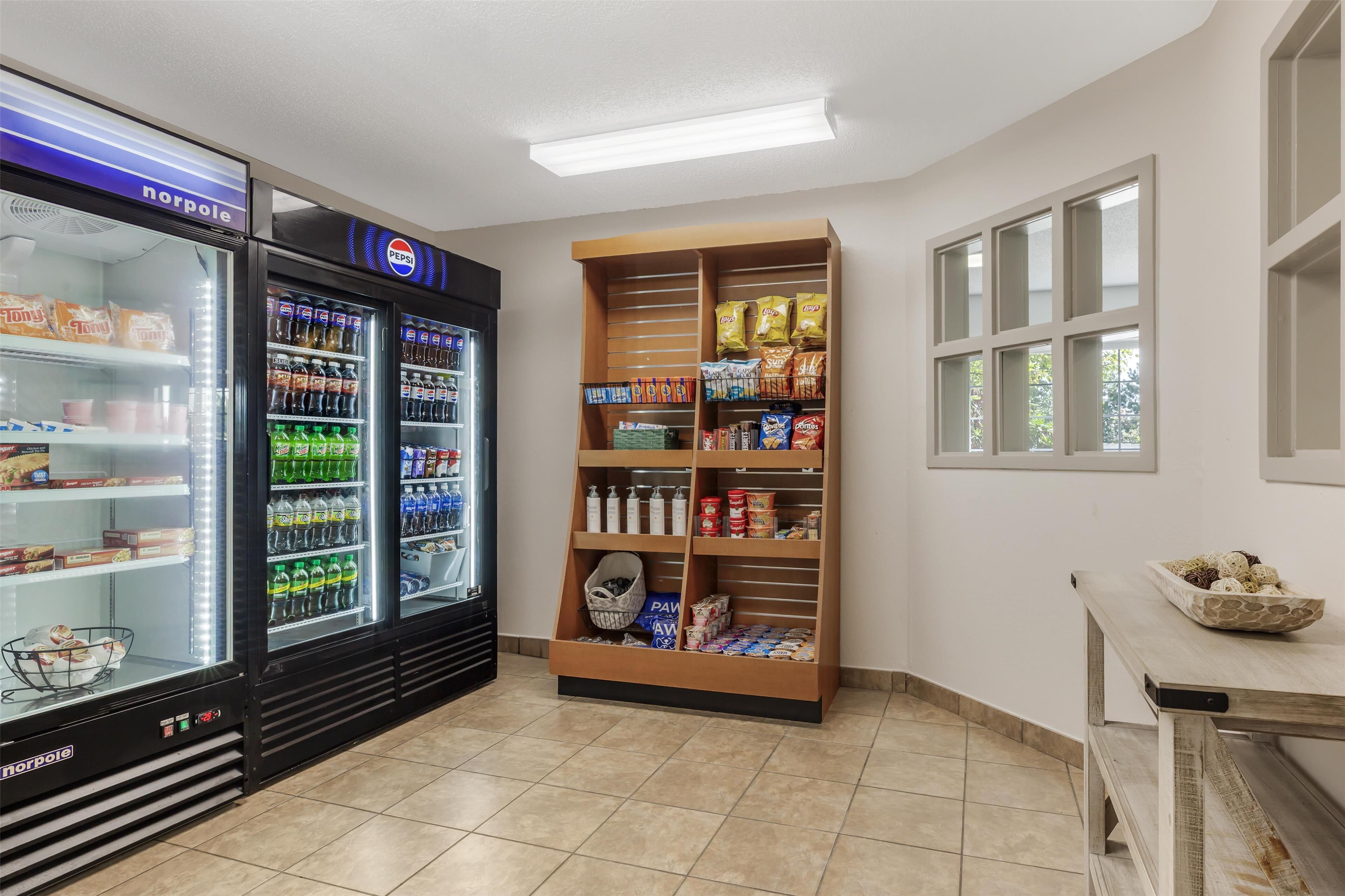 Una pequeña tienda de conveniencia con un refrigerador, estantes llenos de bocadillos y una vitrina.