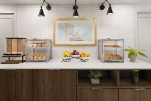A breakfast bar with a variety of breads, fruits, and pastries.