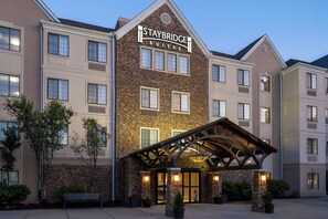 A Staybridge Suites hotel with a stone facade, multiple windows, and a covered entrance area. - Staybridge Suites Boston - Burlington by IHG (Burlington)
