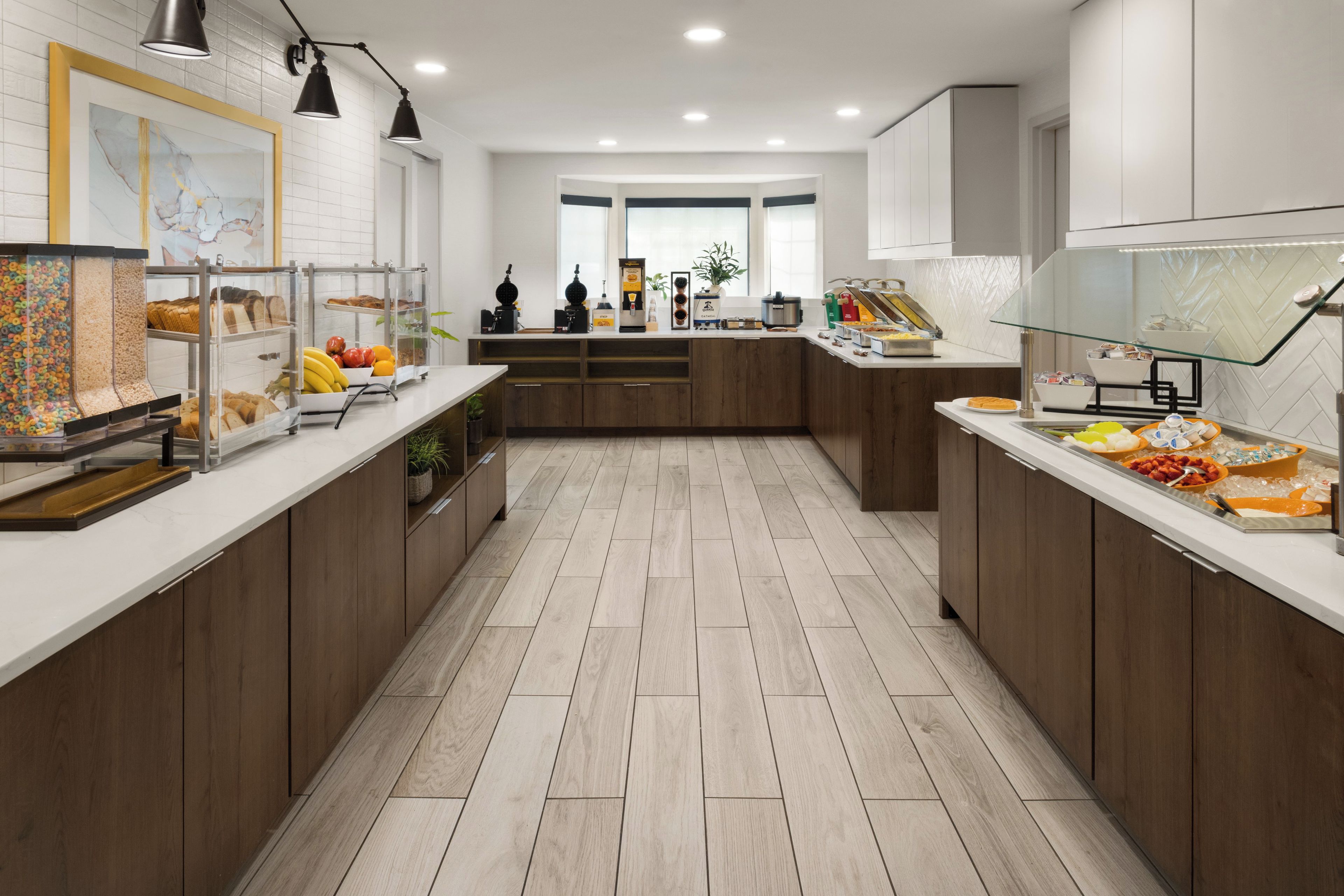 A modern kitchen with a central island, wooden cabinets, and a variety of food items on display.