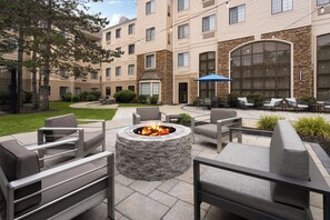 A courtyard with outdoor seating, a fire pit, and a building with stone accents. - Staybridge Suites Boston - Burlington by IHG (Burlington)