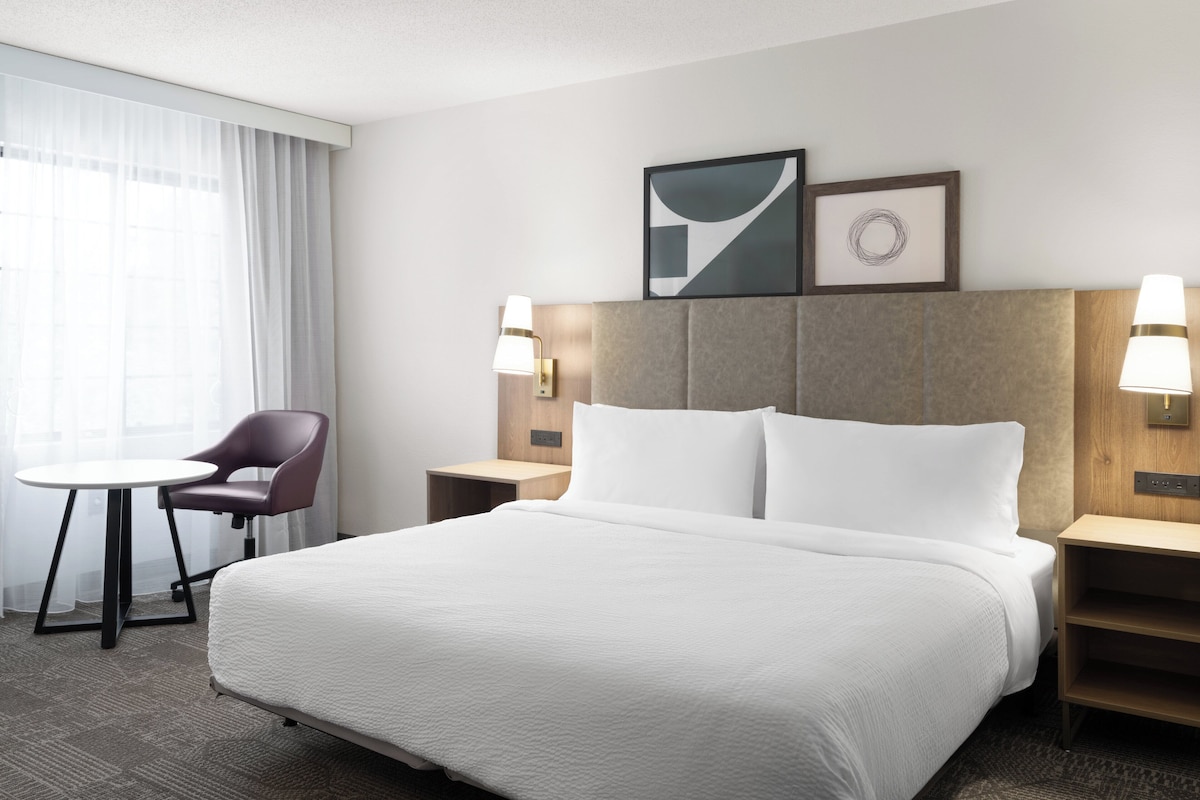A hotel room with a large bed, a chair, a small table, and two bedside lamps.