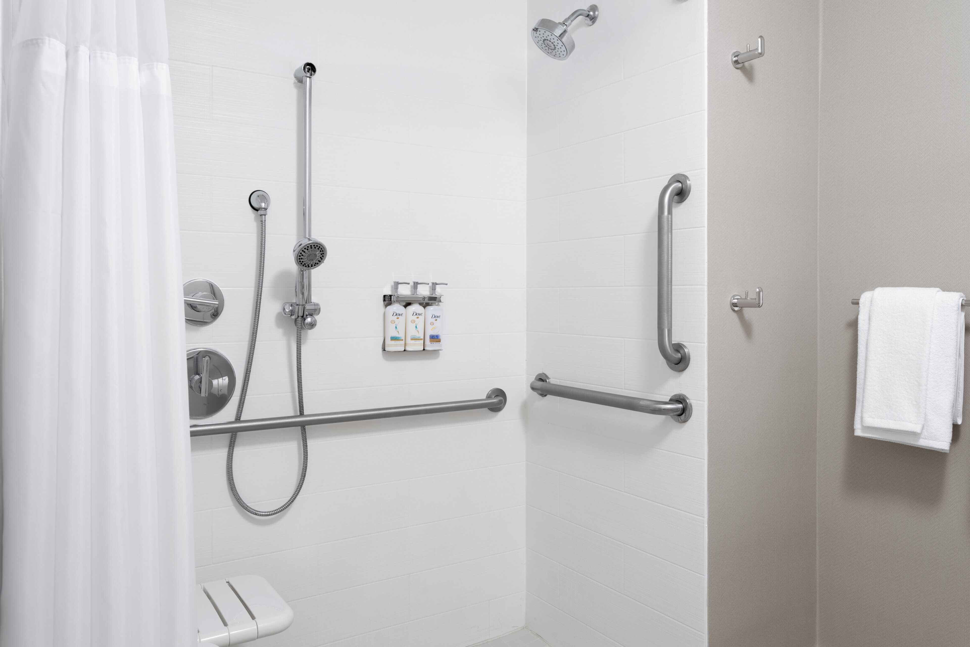 A shower area with a grab bar, a handheld showerhead, and a handheld showerhead with a hose.