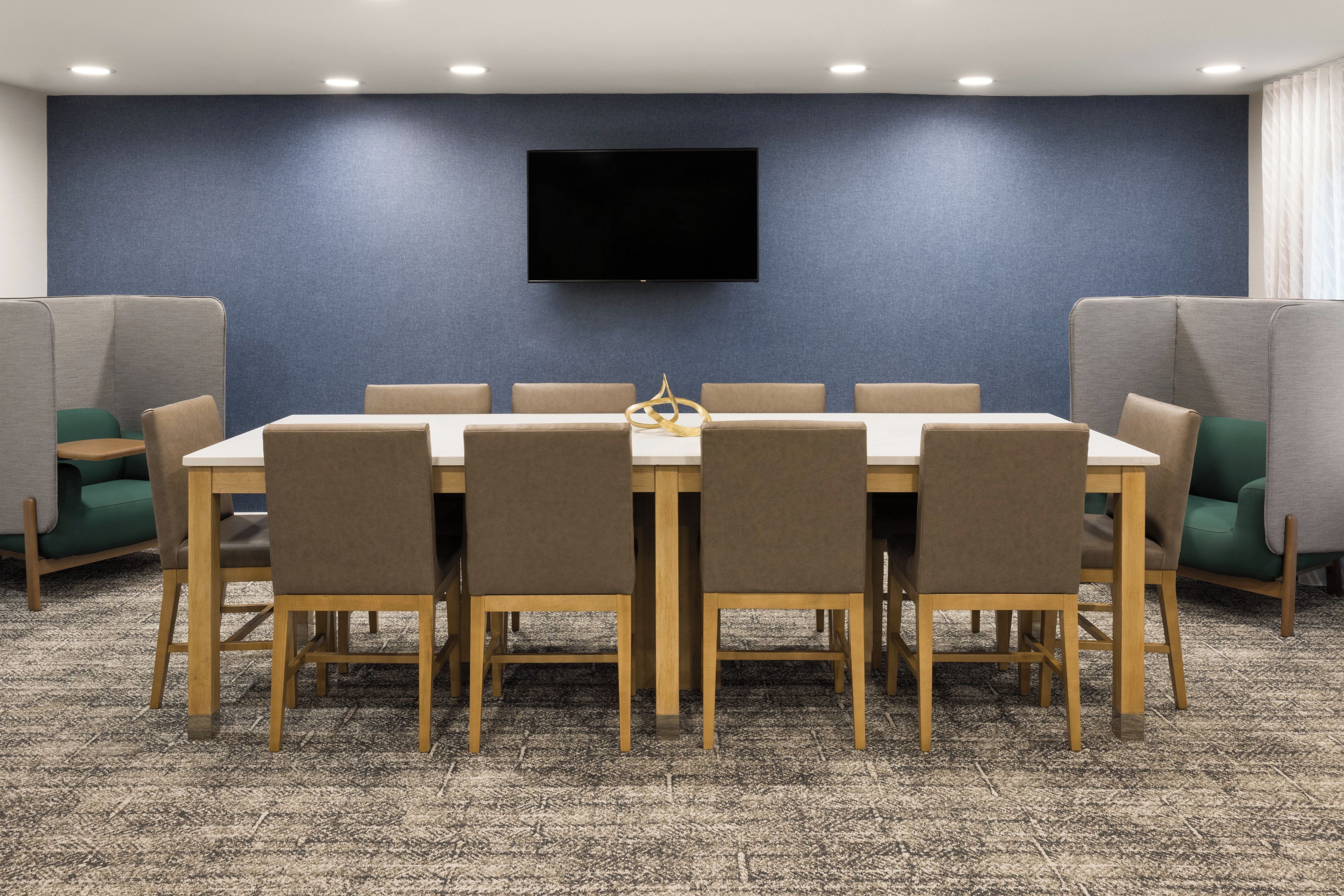 A conference room with a long table, chairs, a flat-screen TV mounted on the wall, and partition walls.