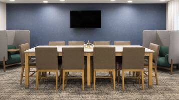 A conference room with a long table, chairs, a flat-screen TV mounted on the wall, and partition walls.