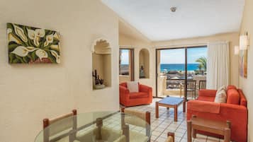 A room with a glass table, red sofas, and a view of the ocean.
