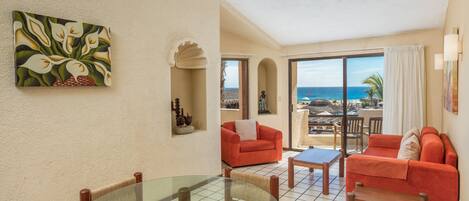 A room with a glass table, red sofas, and a view of the ocean.