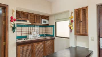 Une cuisine avec des meubles de rangement en bois, un four à micro-ondes, un évier et une fenêtre avec des volets.