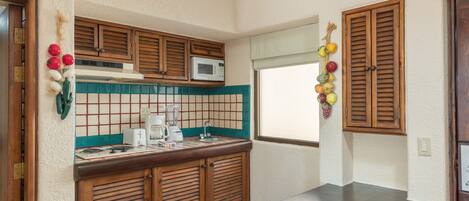 A kitchen with wooden cabinets, a microwave, a sink, and a window with shutters.
