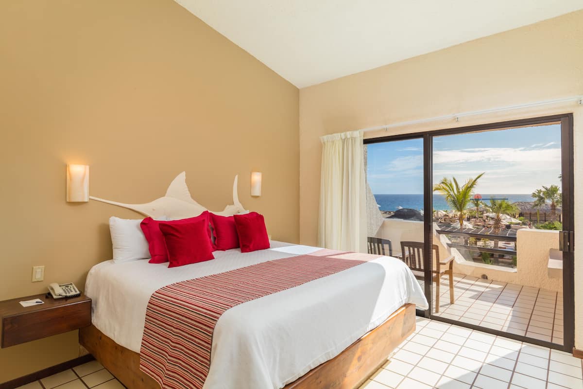 A hotel room with a large bed, a view of the beach, and a balcony with a chair.