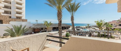 A balcony with a table and chairs, overlooking a resort area with palm trees and a pool.
