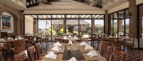 A restaurant with a high ceiling, exposed beams, and large windows overlooking a patio area.