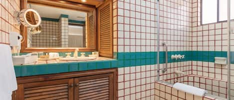 A bathroom with a wooden vanity, a mirror, a shower, and tiled walls.