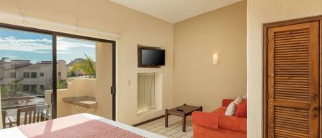 A hotel room with a bed, a sofa, a TV, and a balcony with a view of buildings.