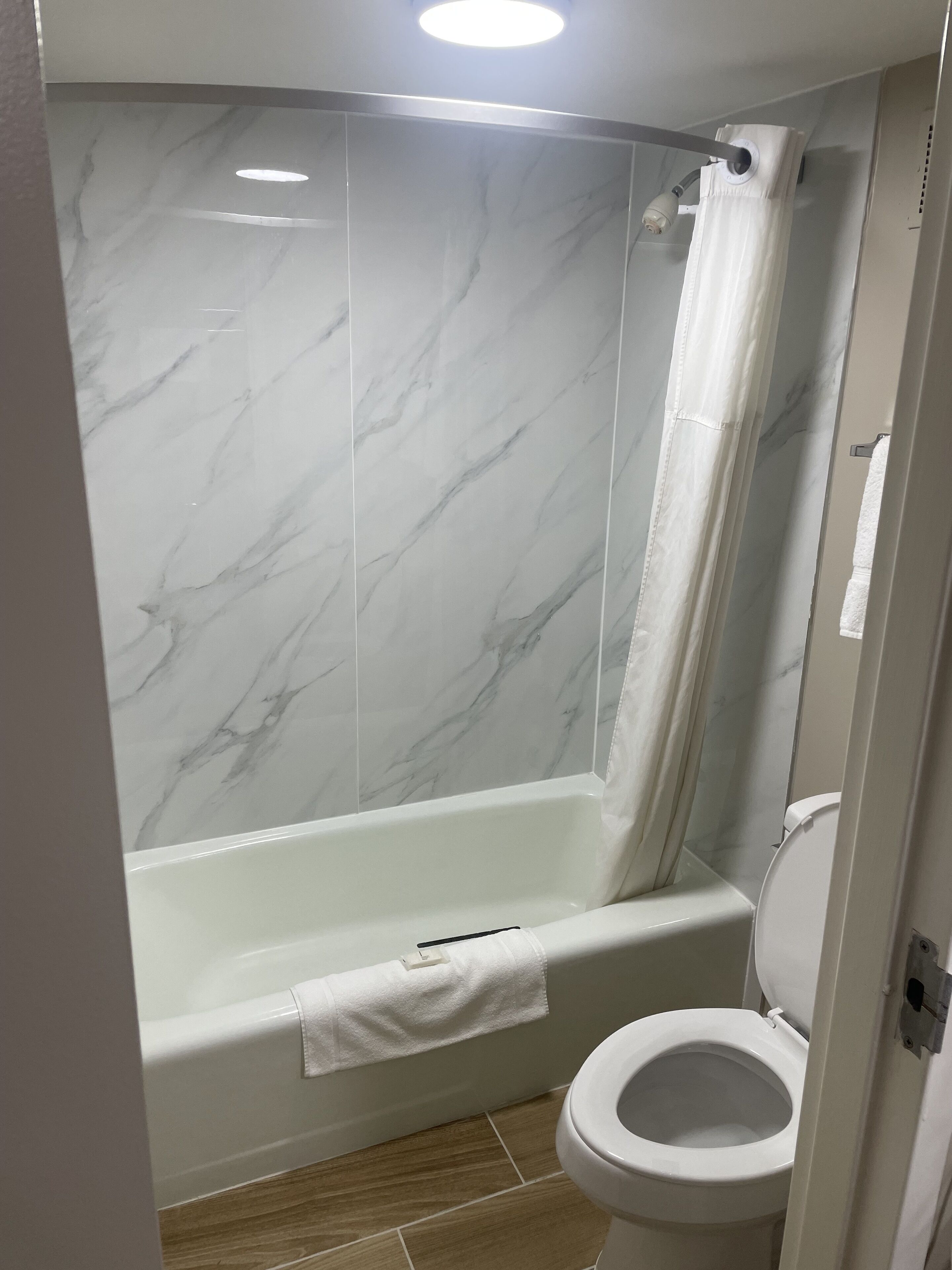 A bathroom with a marble shower wall, a bathtub, and a toilet.