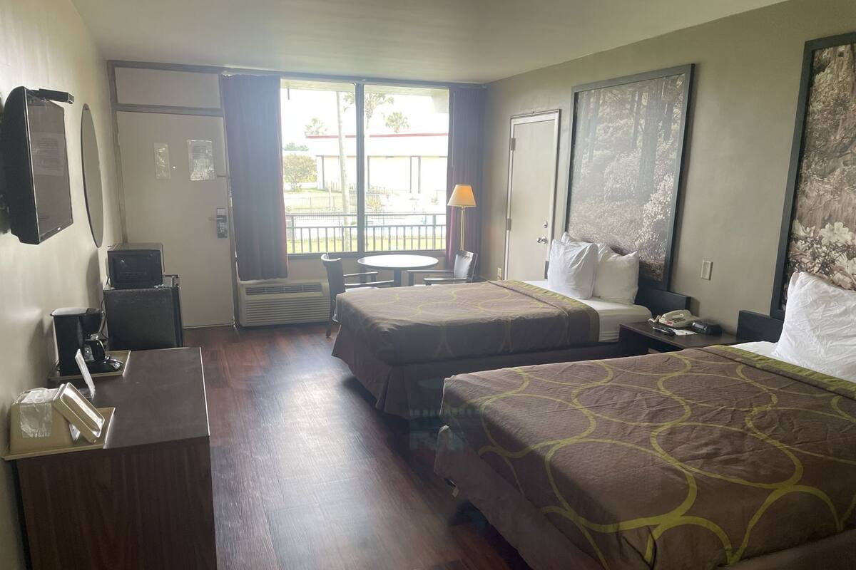 A hotel room with two beds, a desk, a chair, a TV, and a window with a view of the outside.