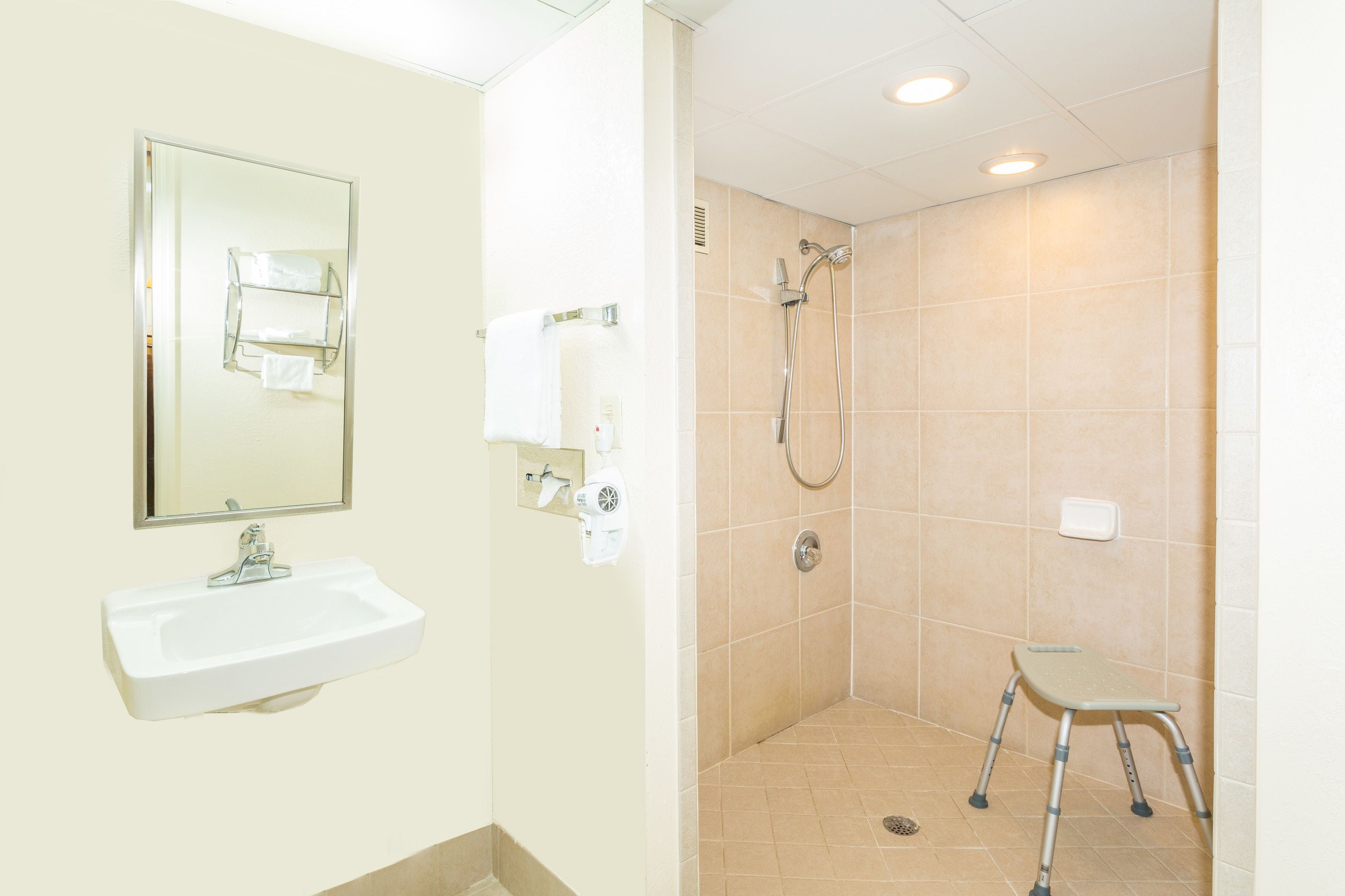 A bathroom with a sink, mirror, towel rack, shower, and a step stool.