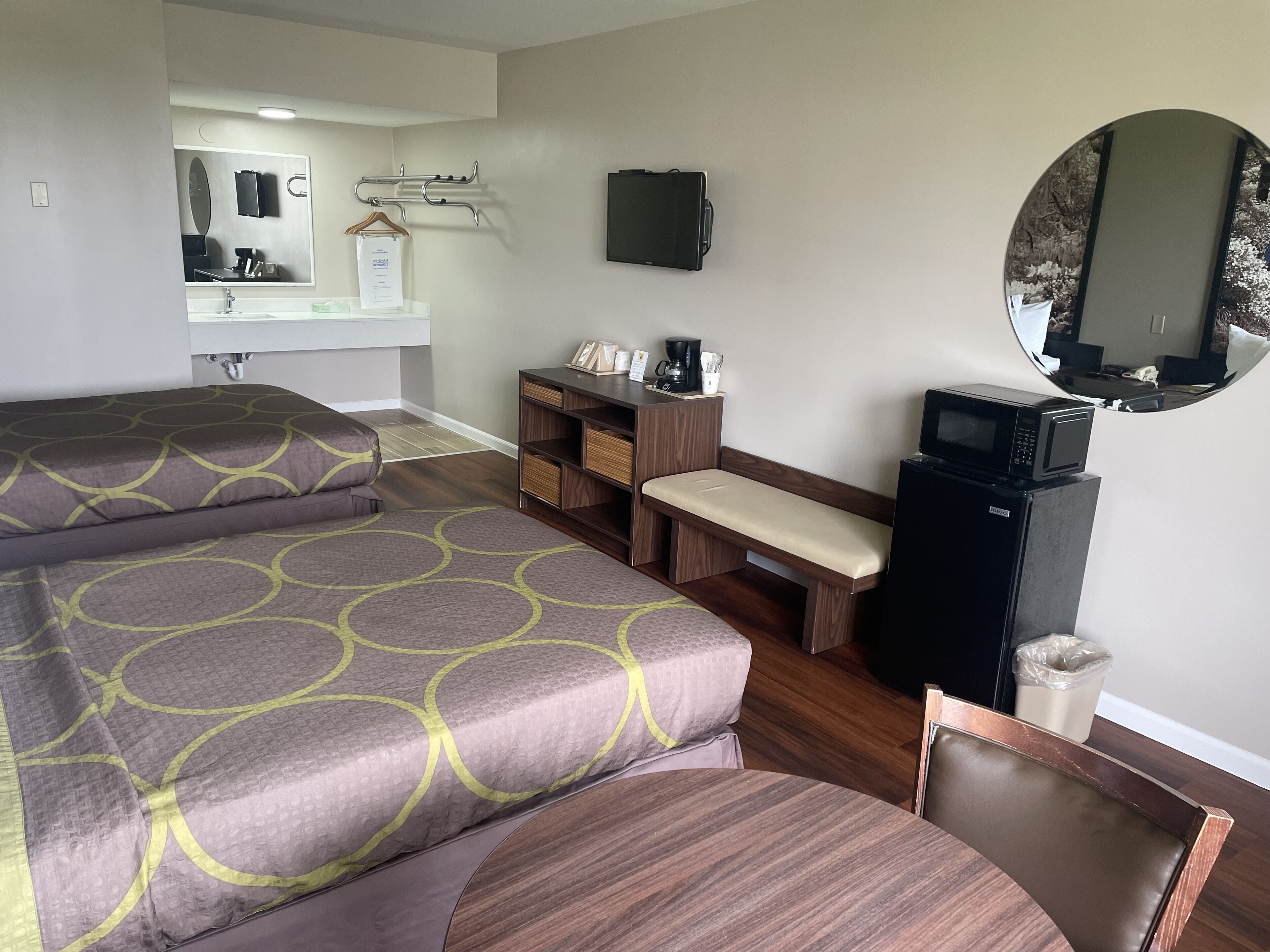 A hotel room with a bed, a small desk, a microwave, and a mirror.