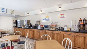 Un área de desayuno con mesas y sillas, una máquina de café y un cartel en la pared que anuncia el desayuno Daybreak.