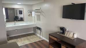 Un baño moderno con lavamanos, espejo, toallero y televisor montado.