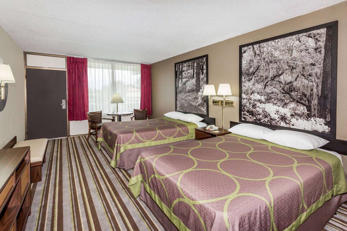 A hotel room with two beds, a desk, a chair, and a large window with curtains.