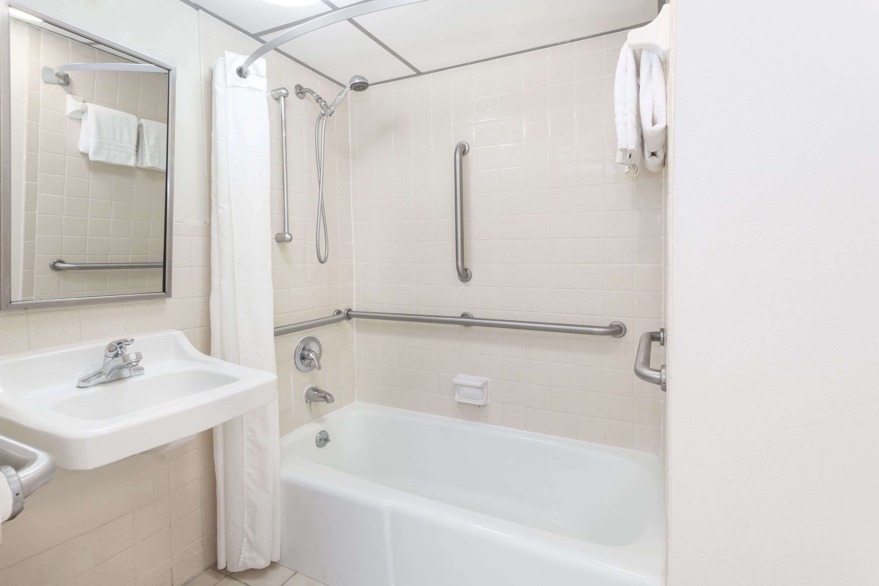 A bathroom with a sink, mirror, bathtub, and grab bars.