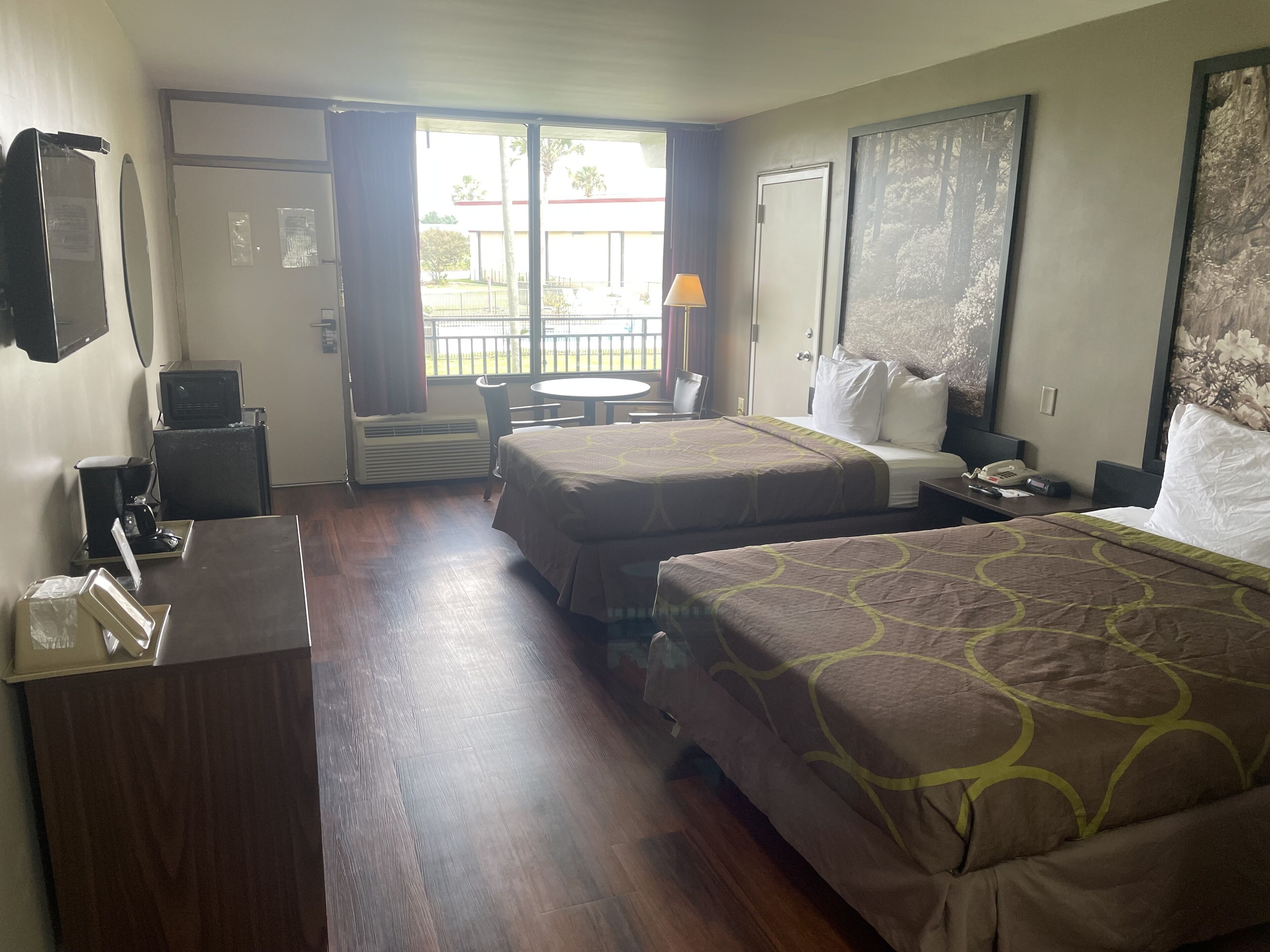 Een hotelkamer met twee bedden, een bureau, een stoel, een klein tafeltje, een lamp en een raam met uitzicht.
