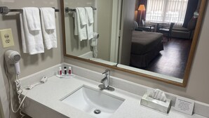 Un baño de hotel con un lavamanos blanco, un espejo, un secador de pelo y un perchero para toallas.