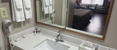 A hotel bathroom with a white sink, a mirror, a hairdryer, and a towel rack.