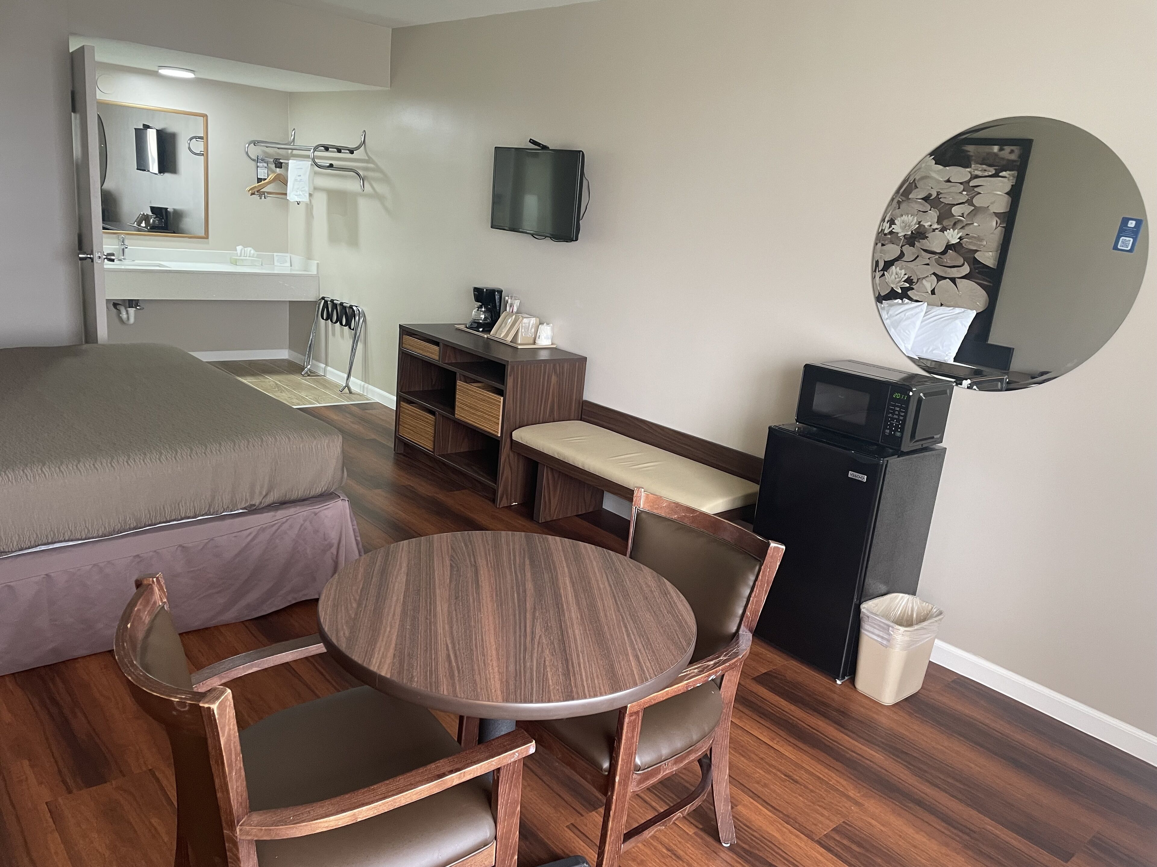 Habitación de hotel con cama, escritorio, silla, mesita, televisor, microondas y cesto de basura.