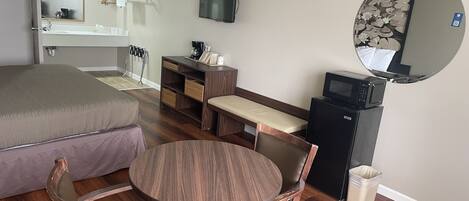 Habitación de hotel con cama, escritorio, silla, mesita, televisor, microondas y cesto de basura.