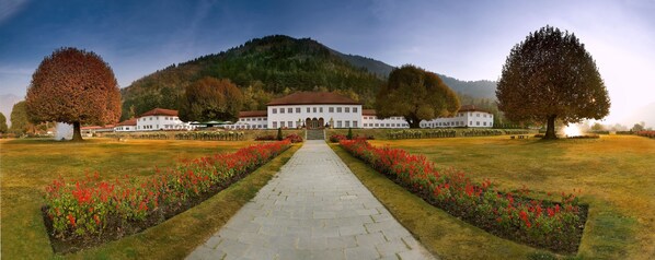 A large white building with a symmetrical facade, a central entrance, and a surrounding garden with red flowers and trees. - The Lalit Grand Palace Srinagar (Srinagar)