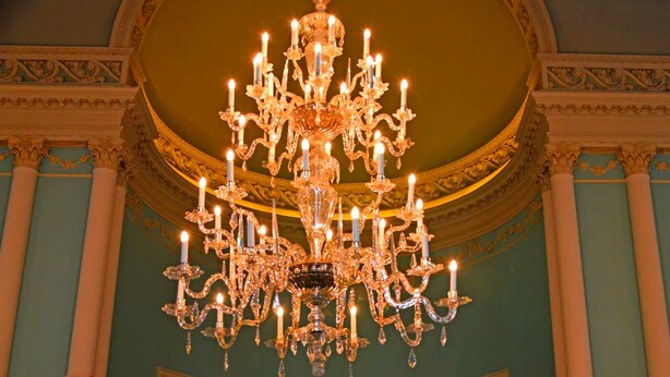 A grand chandelier with multiple candle-like lights, ornate columns, and a balcony railing in a room with teal walls and classical architectural details. - The Lalit Grand Palace Srinagar (Srinagar)