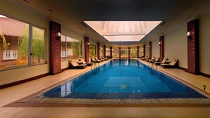 An indoor swimming pool with a skylight, sun loungers, and a view of the outside. - The Lalit Grand Palace Srinagar (Srinagar)