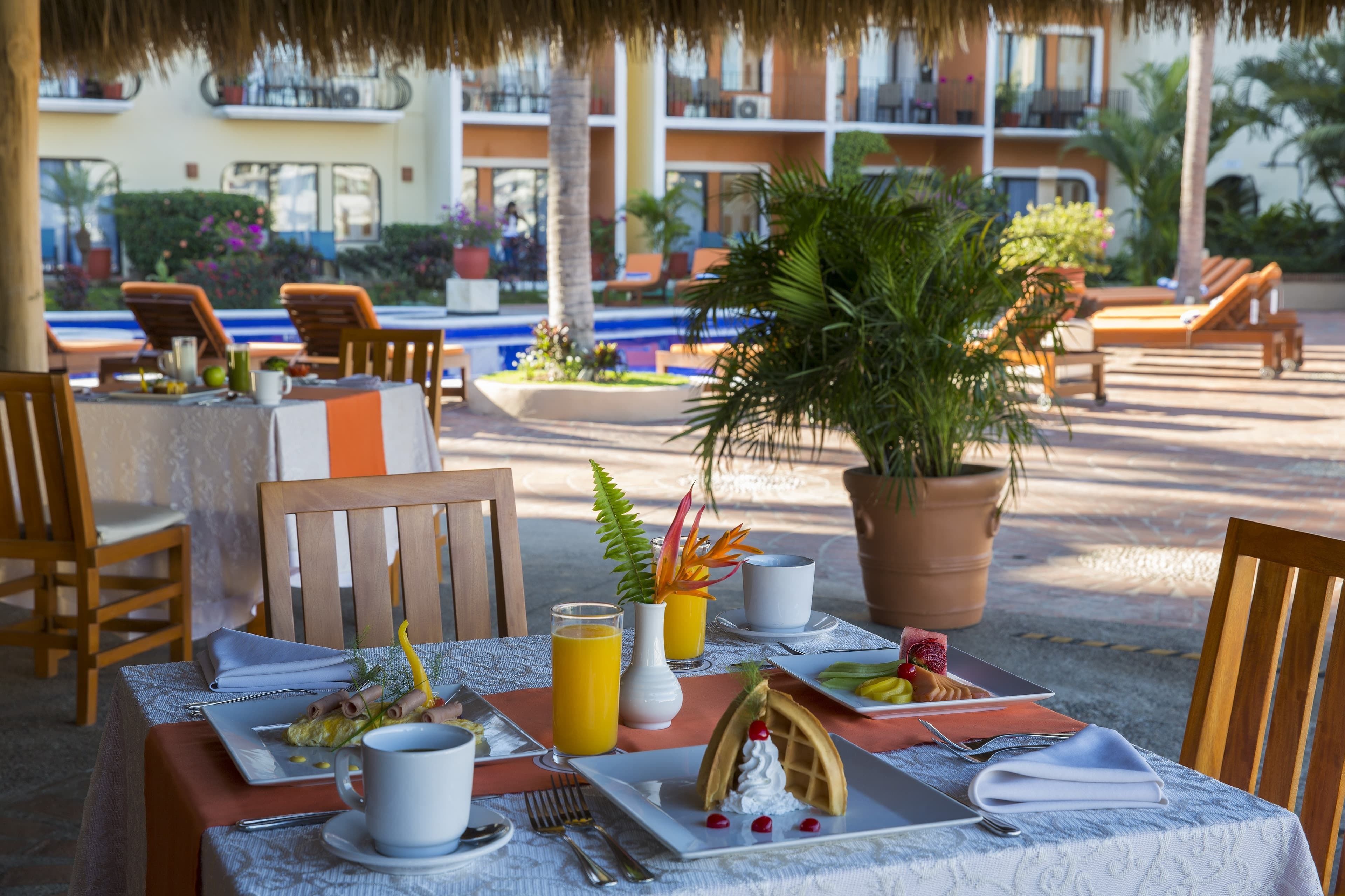 Un espace de restauration en plein air avec des tables préparées pour le petit-déjeuner, comprenant des assiettes de nourriture, des boissons et un gaufre.