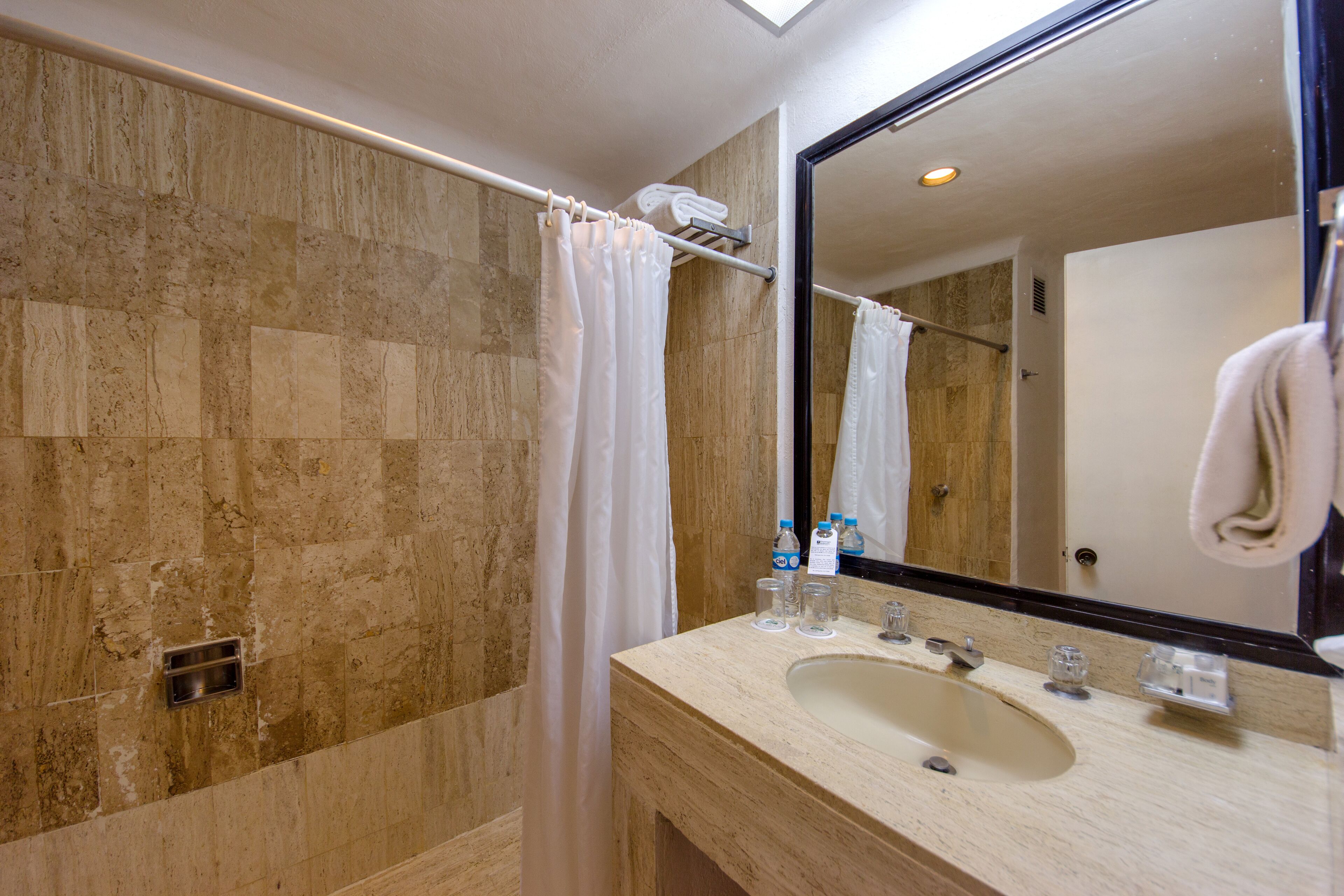 A bathroom with a marble wall, a shower curtain, a sink with a mirror, and a towel rack.
