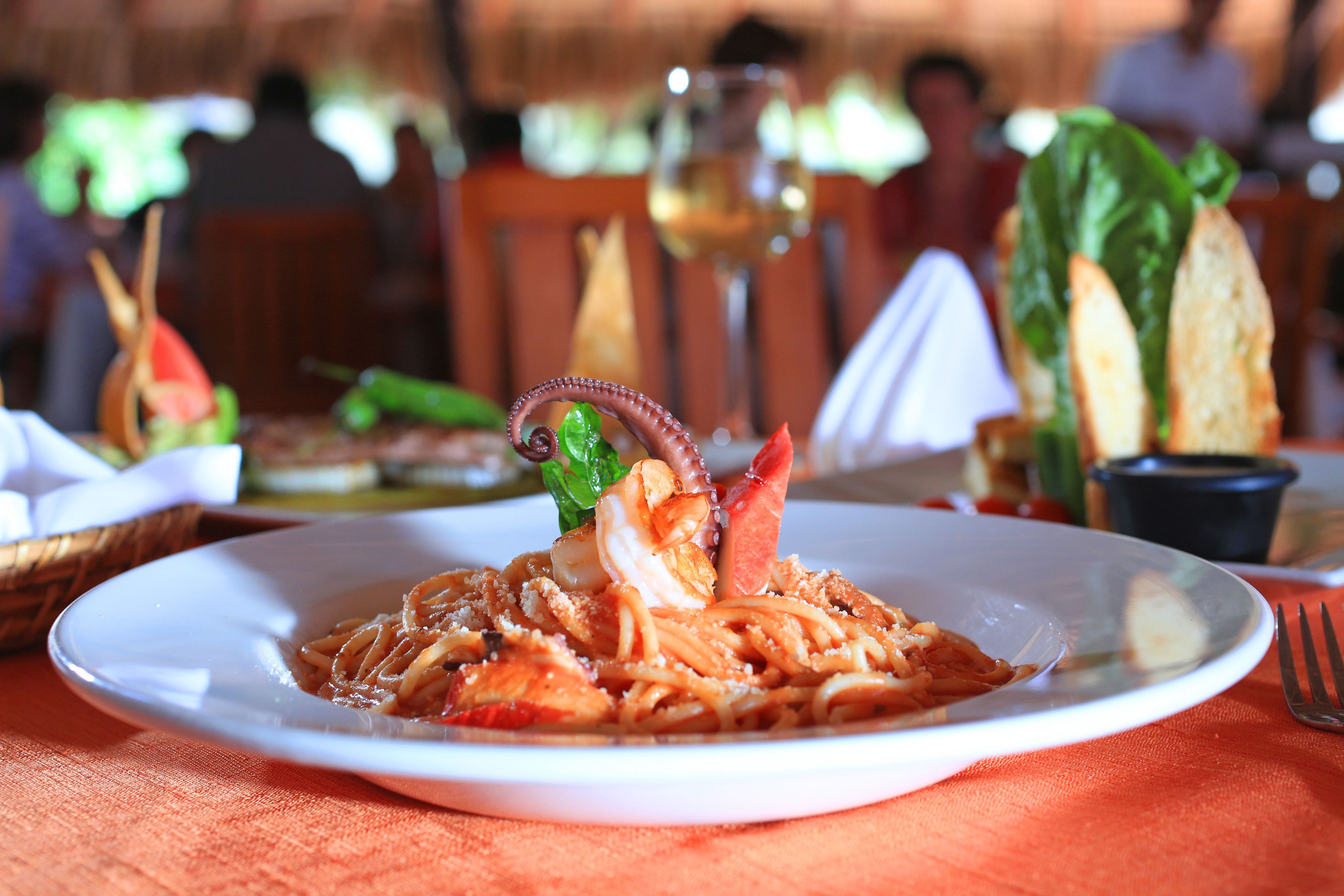 A plate of pasta with seafood and a glass of wine on a table.
