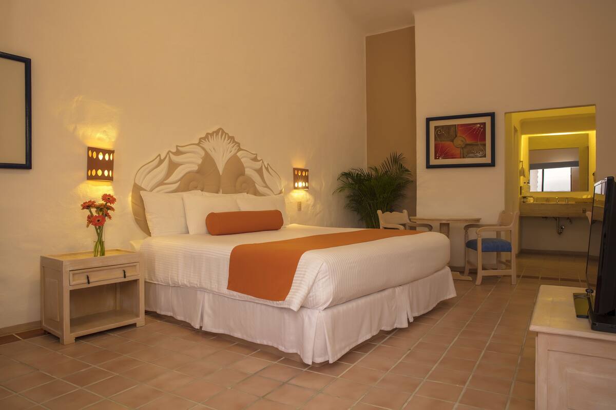 Une chambre d’hôtel avec un grand lit, des tables de chevet, un bureau, une chaise, une télévision et un miroir.