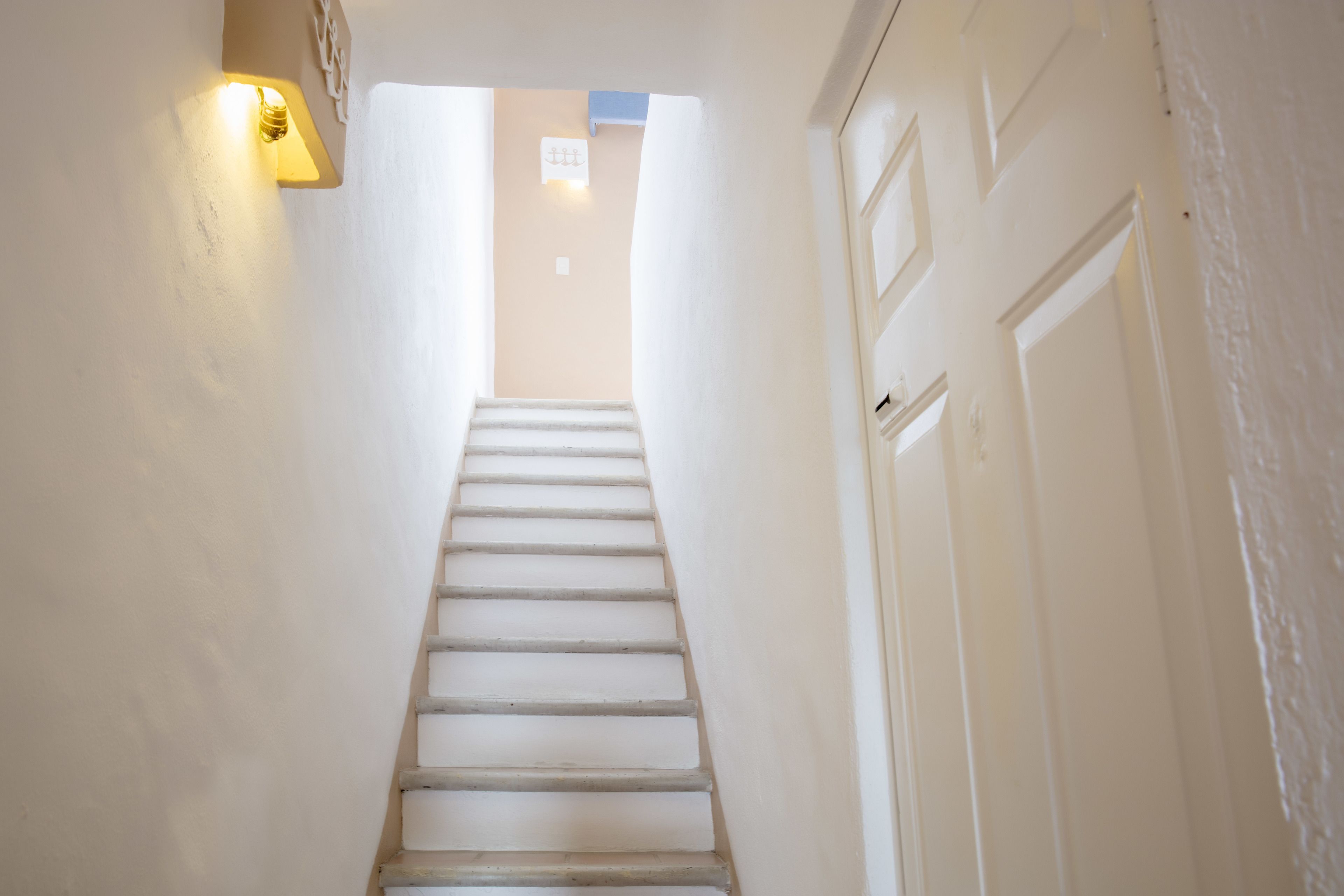 Una escalera blanca que conduce a una puerta, con un accesorio de luz en la pared.